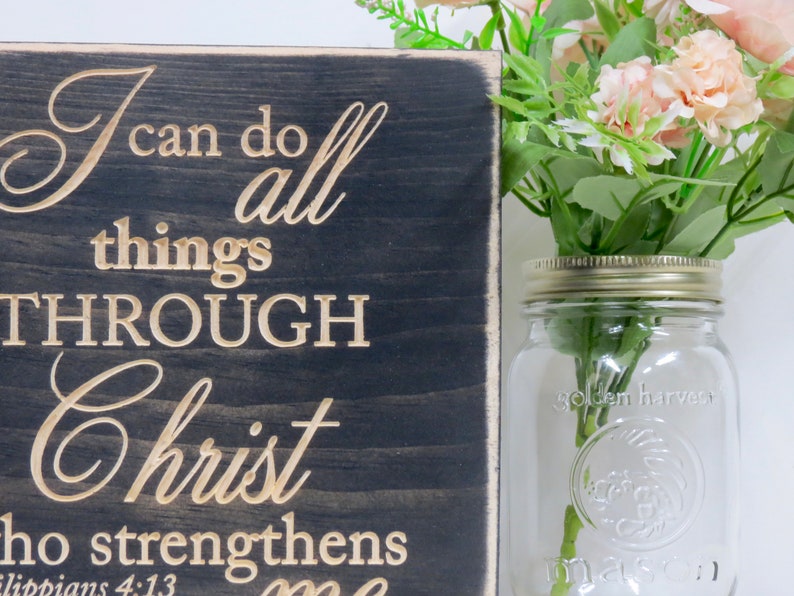 May include: A dark wood sign with the words "I can do all things through Christ who strengthens me" in gold lettering. The scripture reference "Philippians 4:13" is also included in gold lettering.