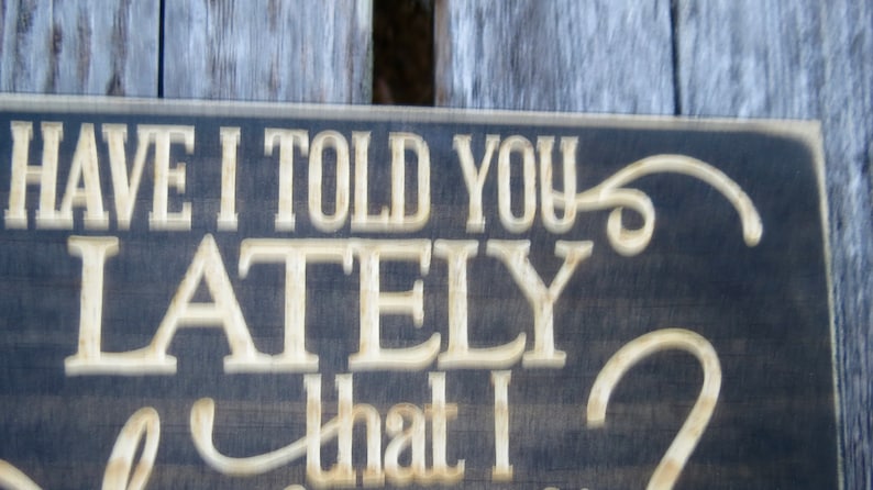 May include: A dark wood sign with white lettering that reads "Have I told you lately that I love you?" The sign has a decorative flourish at the end of the sentence.