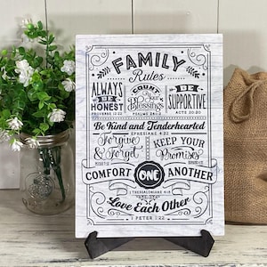 May include: A white wood sign with black text that reads "Family Rules" and includes several Bible verses. The sign is on a black easel.
