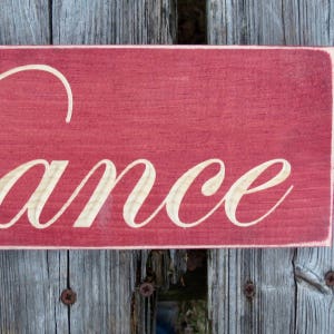 May include: A red wooden sign with the word "dance" written in white paint.