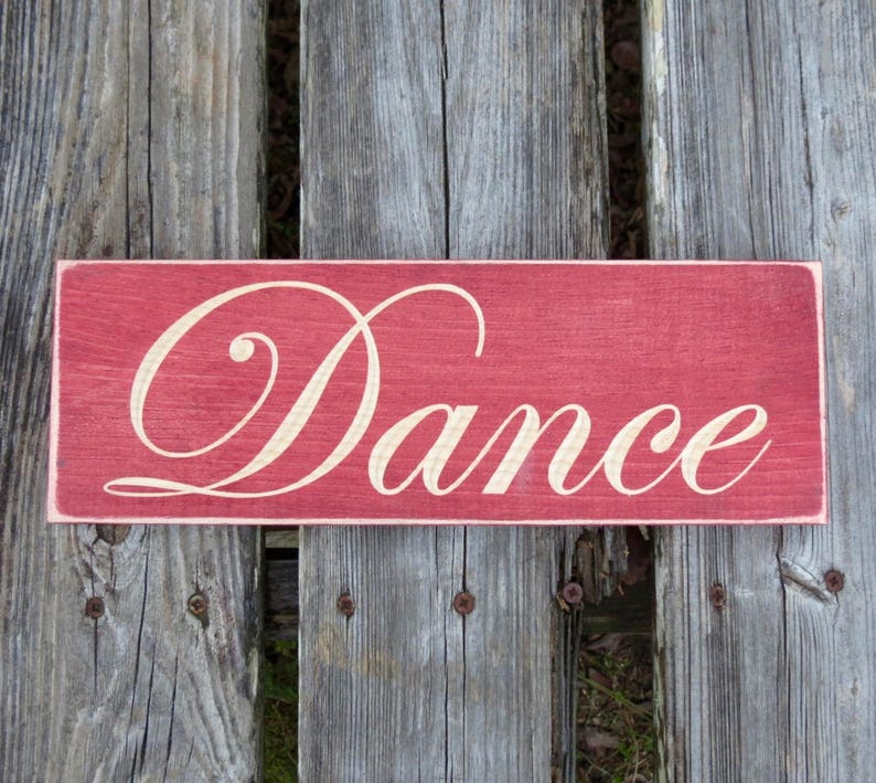 May include: A red wooden sign with the word "Dance" written in white cursive lettering.