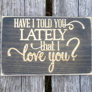 May include: A dark brown wooden sign with the text "Have I told you lately that I love you?" in gold lettering.