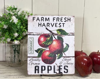 May include: A white sign with the text "FARM FRESH HARVEST" and "APPLES" in black lettering. The sign also features a drawing of red apples on a branch with green leaves. The text "ORGANIC", "Locally Grown", and "Sweet & Juicy" are also on the sign.