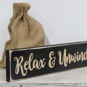 May include: Black wooden sign with white trim and the text "Relax & Unwind" in a cursive font.