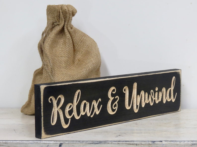 May include: Black wooden sign with white trim and the text "Relax & Unwind" in a cursive font.