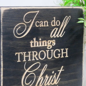 May include: A black wooden sign with white lettering that reads "I can do all things through Christ".