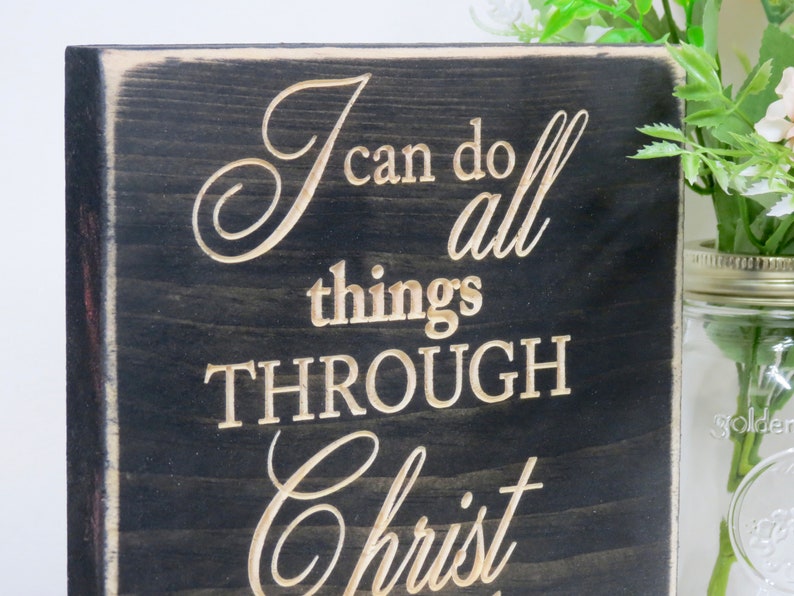 May include: A black wooden sign with white lettering that reads "I can do all things through Christ".