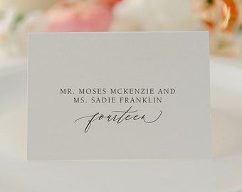 May include: White place card with black text. The text reads "Mr. Moses Mckenzie and Ms. Sadie Franklin fourteen".