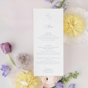 May include: A wedding menu card with the initials "RL" at the top, surrounded by flowers. The menu lists a summer salad, seared chicken, beef tenderloin, blackened salmon, and wedding cake. The card is surrounded by yellow, purple, and white flowers.