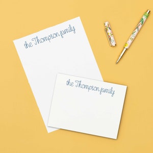 May include: A white notepad and flat stationery cards with the text "the Thompson family" printed in blue ink. The notepad and cards are on a yellow background. The text "invited by LAMAWORKS" is printed in black ink at the bottom of the image.