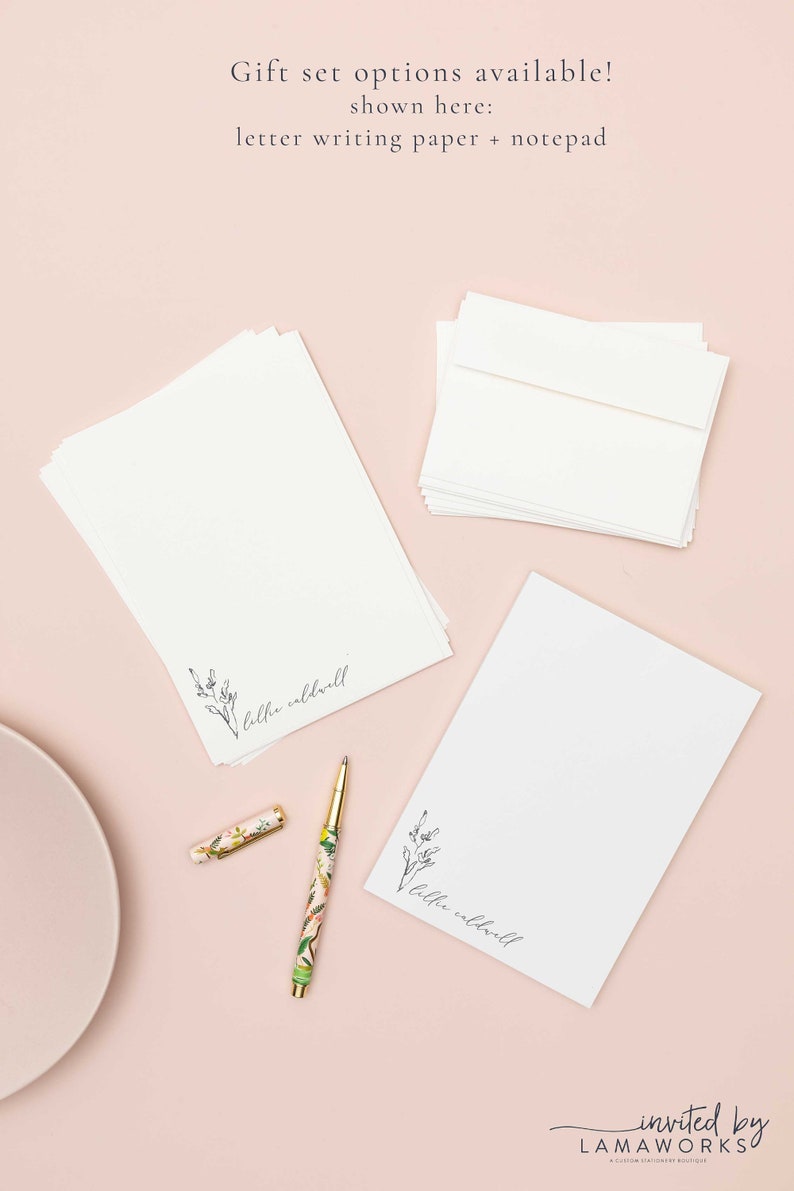 Op de afbeelding: Een set gepersonaliseerd briefpapier met briefpapier en een notitieblok. Het papier heeft een eenvoudig bloemenmotief en de naam "lilhe caldwell" gedrukt aan de onderkant. Het notitieblok heeft hetzelfde ontwerp en dezelfde naam. Het briefpapier wordt gepresenteerd op een roze oppervlak met een bloemenpen.