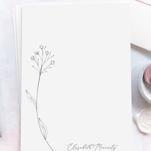 May include: A white card with a simple black line drawing of a flower with a few small buds. The card has the name "Elizabeth Moriarty" written in cursive at the bottom.