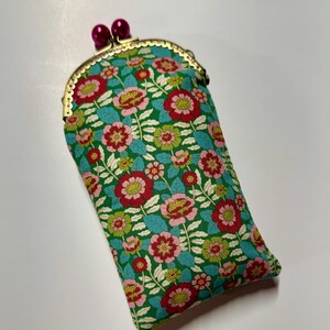 May include: A rectangular fabric pouch with a green background featuring a floral pattern of red, pink, and light green flowers with teal leaves. The pouch has a gold-toned metal kiss-lock frame closure topped with two round, dark pink beads.