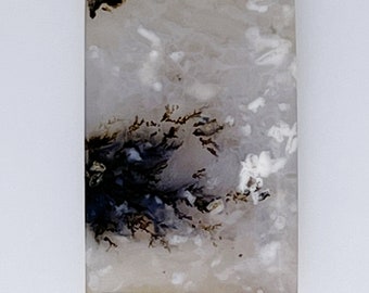 May include: A white agate cabochon with black and brown dendritic patterns. The stone has a smooth, polished surface.