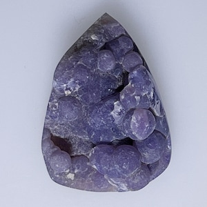 May include: A purple agate cabochon with a unique, bubbly texture. The stone has a deep purple color with lighter purple and white accents.