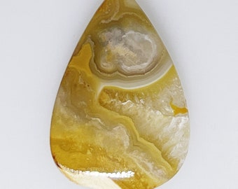 May include: A teardrop-shaped, yellow and white agate cabochon with a swirling pattern. The stone has a smooth, polished surface.