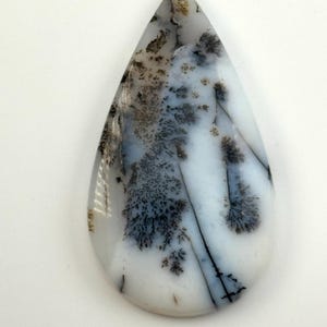 May include: A teardrop-shaped cabochon of dendritic agate with a white base and black dendritic patterns.