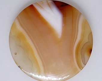 May include: A round, flat agate stone with a white and brown swirling pattern. The stone has a smooth, polished surface.