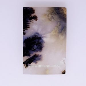 May include: A rectangular dendritic agate cabochon featuring a translucent off-white base with dark brown and black fern-like inclusions that resemble tree branches or mossy patterns spread across the polished stone surface.