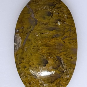 May include: An oval gemstone displaying a distinctive pattern. The stone combines olive green and brown tones, with a textured, brushstroke-like appearance. The polished surface reflects light, emphasizing the natural variations in colour and texture.