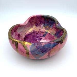 May include: A pink ceramic bowl with a heart-shaped opening and a gold rim. The bowl is decorated with a crackle glaze and gold accents.