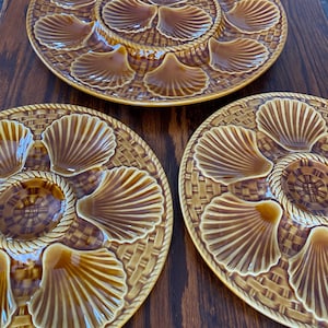 Può includere: Tre piatti per ostriche in ceramica marrone con un design a cesto intrecciato e incavi individuali a forma di conchiglia per servire le ostriche.
