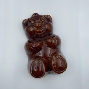 Könnte beinhalten: Glänzende, braune Keramik-Bärenfigur mit lächelndem Gesicht und abgerundeten Merkmalen. Der Bär hat eine glatte, glasierte Oberfläche und ist in einem skurrilen, cartoonartigen Stil gestaltet. Die Figur ist ein dekorativer Artikel.