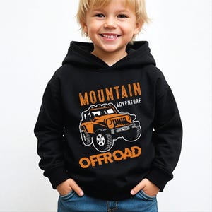 Puede incluir: Sudadera con capucha negra con un gráfico de vehículo todoterreno naranja. El diseño incluye las palabras "MOUNTAIN ADVENTURE OFFROAD" en naranja. La sudadera es usada por un niño.