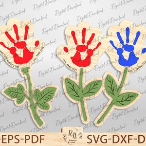 Könnte beinhalten: Drei hölzerne Rosen-Ausschnitte mit Handabdruck-Designs. Die Rosen sind rot, blau und grün. Der Text auf den Rosen lautet "Happy First Mother's Day" und "Love, Annie 2025".