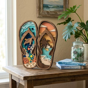 May include: A layered wooden wall art piece shaped like a pair of flip-flops. The left sandal features an underwater ocean scene with a sea turtle, coral, and fish. The right sandal depicts a beach landscape with a palm tree, sand, and sunset.