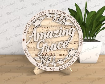 May include: A round wooden sign featuring the words "Amazing Grace" in a decorative font. The sign is adorned with floral designs and a musical note background. The text "Once was lost, but now am found, How sweet the sound, Was blind but now I see" is printed around the edge of the sign.
