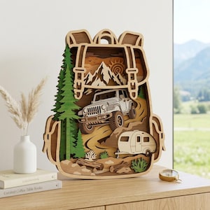 May include: A multi-layered wooden wall art piece shaped like a backpack, featuring a carved scene of a white off-road vehicle towing a small camper trailer through a mountain landscape with green pine trees, brown logs, and a sun design.