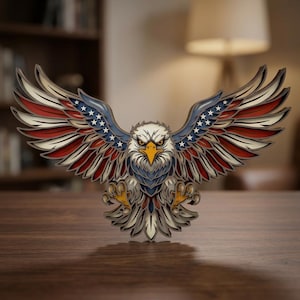 May include: A wooden, layered eagle sculpture with outstretched wings, featuring the American flag's colors: red, white, and blue. The eagle has a stern expression and is perched on a wooden surface. The wings display stars and stripes.