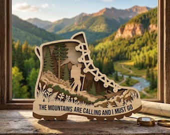 May include: A layered wooden cutout shaped like a hiking boot featuring a silhouette of a hiker with a backpack and walking sticks amidst pine trees and foliage. The text THE MOUNTAINS ARE CALLING AND I MUST GO is printed on the base of the boot.