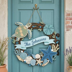 May include: A circular wooden wreath featuring a sea turtle, a starfish, various seashells, and coral accents in shades of blue, green, and cream. A central light blue banner displays the text The Johnsons in dark blue script lettering.