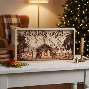 May include: A rectangular wooden nativity scene featuring layered cutouts of the Holy Family, camels, sheep, and angels under a star. The text "Oh Holy night" is carved into the top section. The design uses varying shades of natural wood.