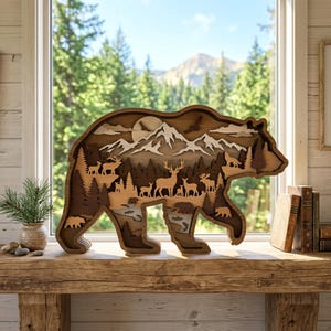 May include: A multi-layered wooden bear-shaped wall art piece featuring a laser-cut forest scene with mountains, a moon, and various wildlife silhouettes including deer, elk, moose, and bears, all rendered in varying shades of natural wood tones.