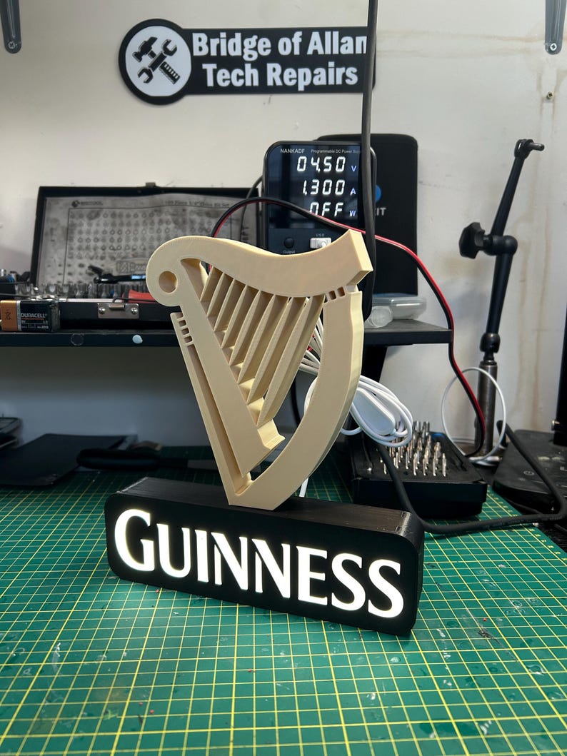 May include: A 3D printed Guinness harp logo with a black base and white LED lights. The logo is illuminated and the word "GUINNESS" is visible on the base.