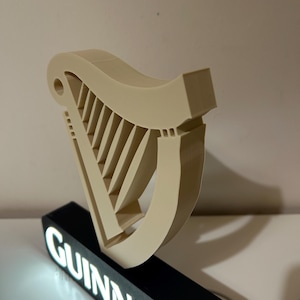 May include: A 3D printed white harp-shaped sign with the word "GUINNESS" in white letters on a black base.