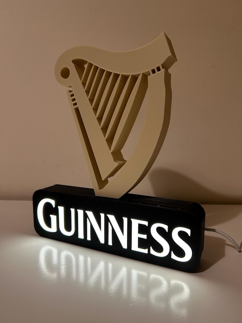May include: A black and white illuminated sign with the word "GUINNESS" in white letters. The sign features a 3D harp in a cream colour.