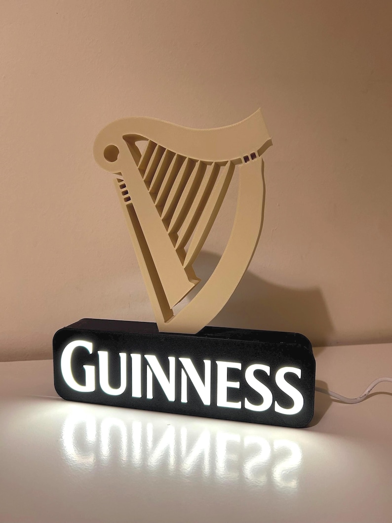 May include: An illuminated sign featuring the Guinness logo. The logo depicts a harp in white, mounted on a black base with the word "GUINNESS" in white lettering.