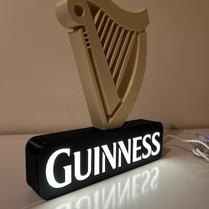 May include: An illuminated Guinness sign with a 3D harp logo and the word "GUINNESS" in white lettering on a black background.
