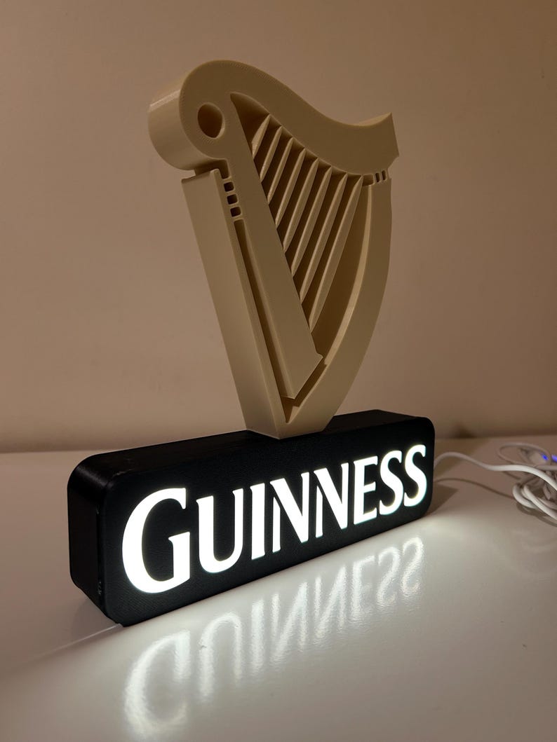 May include: An illuminated Guinness sign with a 3D harp logo and the word "GUINNESS" in white lettering on a black background.