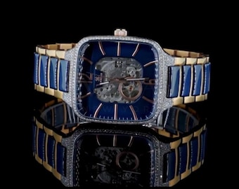 May include: A luxury wristwatch with a square, blue face and a skeleton design. The watch features a gold and blue band, and is encrusted with small, sparkling stones around the face. The watch is displayed on a reflective black surface.