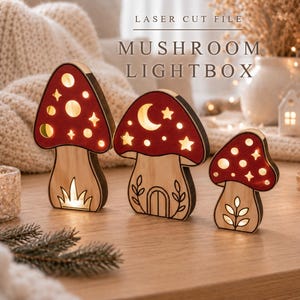 May include: Three wooden mushroom-shaped lightboxes with red caps and light-colored stems. The caps feature cutouts of stars, circles, and a crescent moon. The stems have engraved details including a door, leaves, and grass. Text reads LASER CUT FILE MUSHROOM LIGHTBOX.