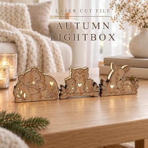 Könnte beinhalten: Drei lasergeschnittene Lichtboxen aus Holz mit Tiermotiven. Die erste zeigt einen Bären mit Jungtier, die zweite eine Eule mit zwei Jungen und die dritte ein Reh mit Kitz. Jedes Stück verfügt über herzförmige Ausschnitte und eine Innenbeleuchtung.