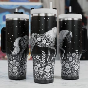 Puede incluir: Tres vasos de acero inoxidable negro con tapas y asas blancas. Cada vaso presenta una silueta blanca de un caballo con diseños florales sobre un fondo negro.