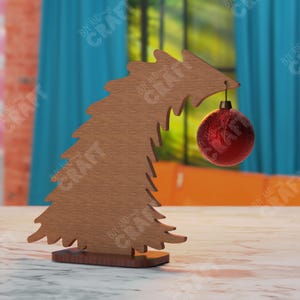 May include: A wooden Christmas tree-shaped ornament holder with a red ornament hanging from the top. The tree is brown and has a decorative design. The ornament is round and has a shiny finish. The holder is on a table.