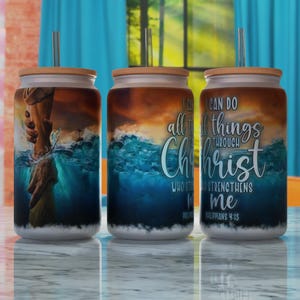 May include: Three stainless steel tumblers with lids and straws. The tumblers feature a blue and orange sunset scene with waves and a hand reaching out from the water. The text on the tumblers reads "I can do all things through Christ who strengthens me Philippians 4:13".