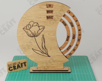 May include: A crescent moon-shaped wooden perpetual calendar featuring a laser-engraved tulip illustration. The calendar displays the date 31 NOV SAT, with rotating rings for months and days. Material thickness is 3mm to 3.2mm.